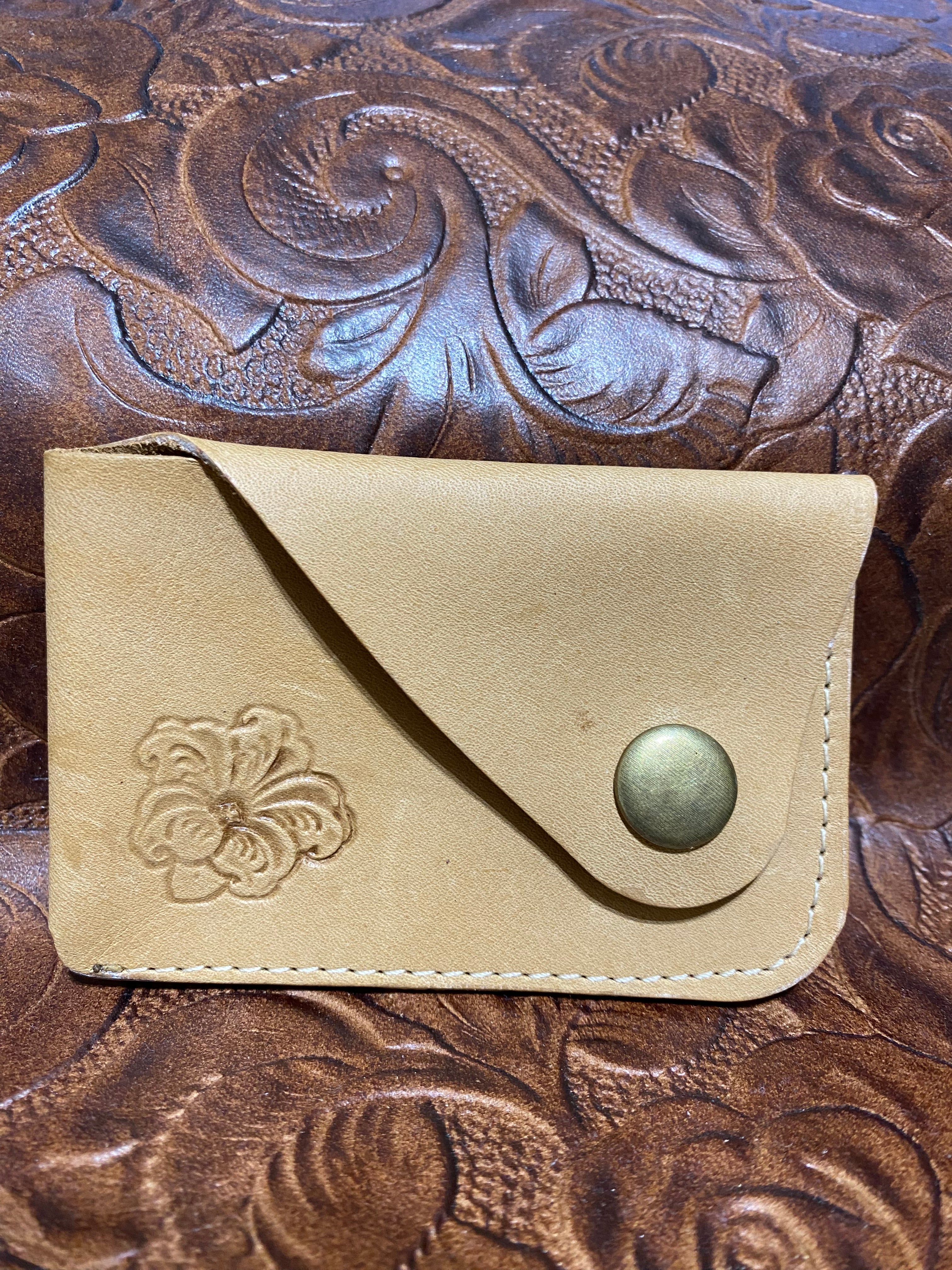 Beige leather wallet with floral embossing on a textured brown leather background